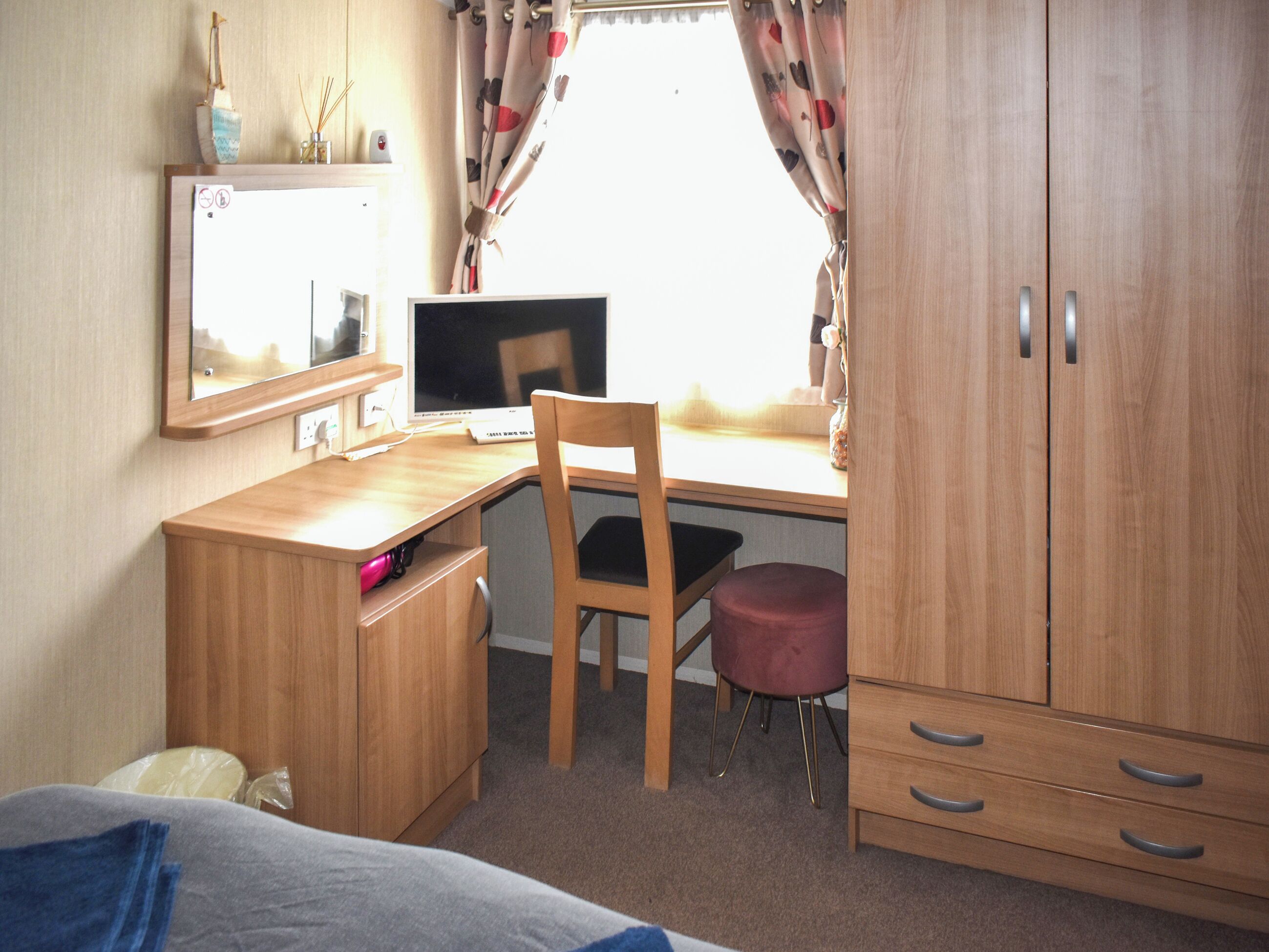 Een slaapkamer met een houten bureau, een stoel, een bed en een kledingkast.