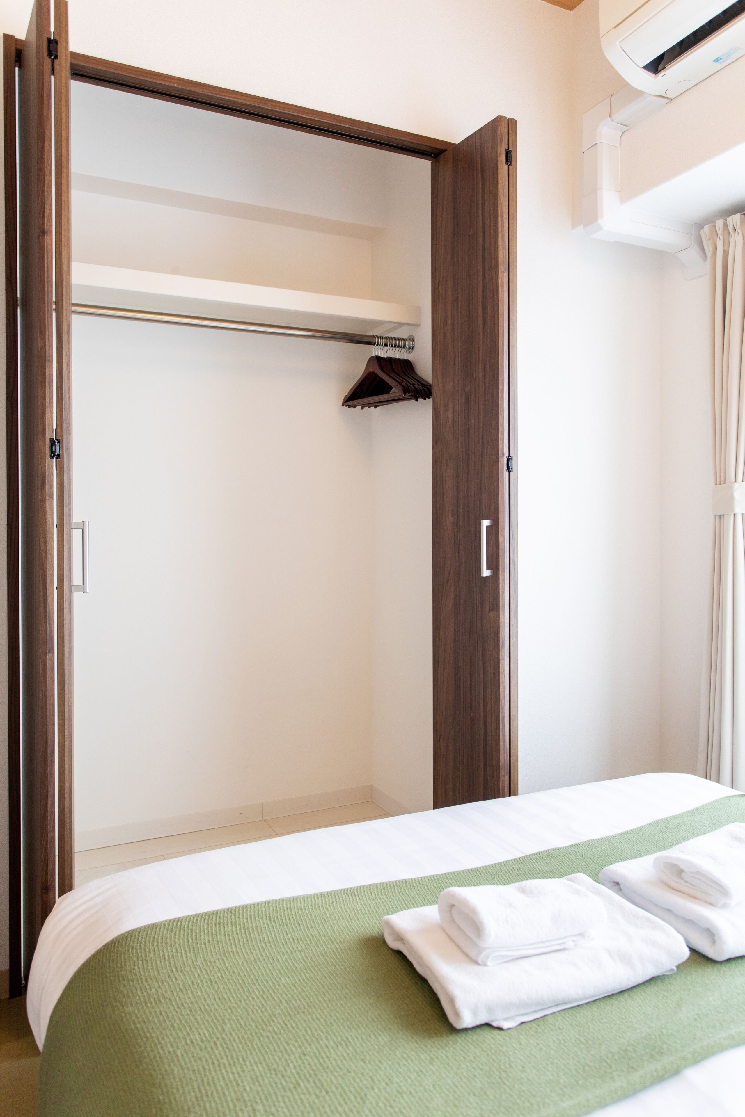 A hotel room with a bed, a green bedspread, a wooden wardrobe, and a hanging towel rack.
