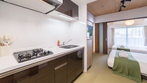 Een moderne keuken met een gasfornuis, een spoelbak en witte aanrechtbladen. Er is een slaapkamer met een bed en een groene plaid.