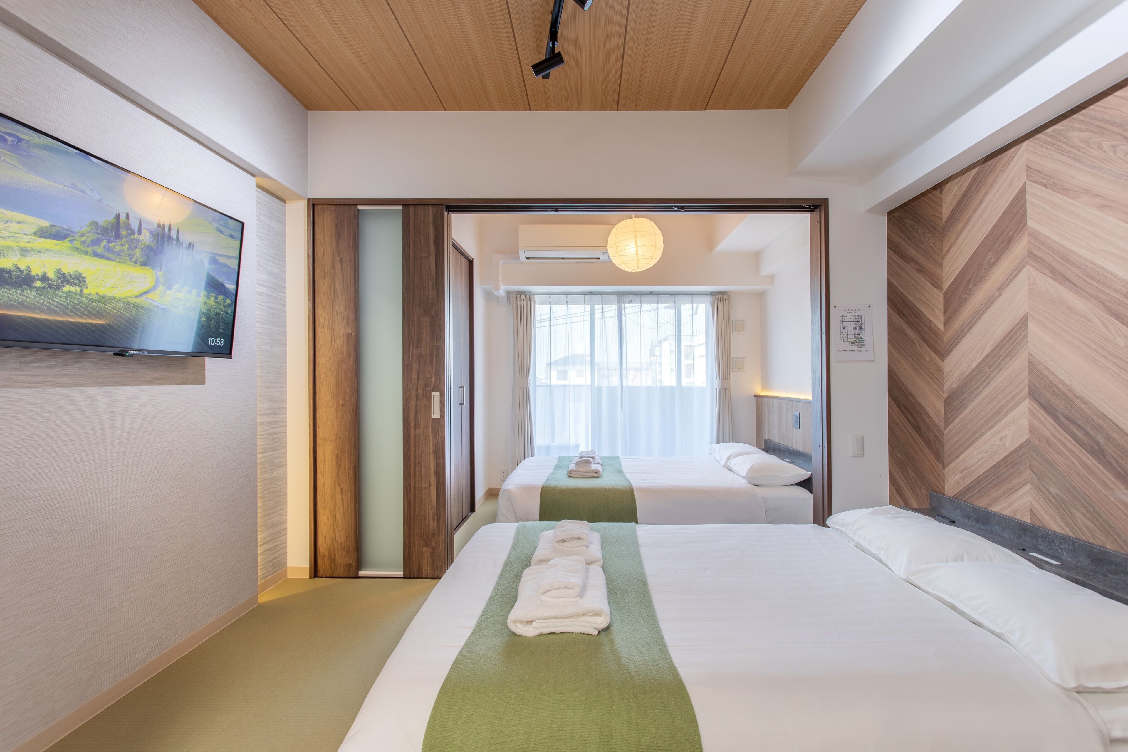 A hotel room with two beds, a TV, a wooden ceiling, and a view through an open door.