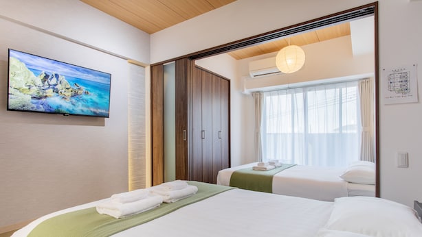 Habitación de hotel con dos camas, televisión, armario y ventana con cortinas.