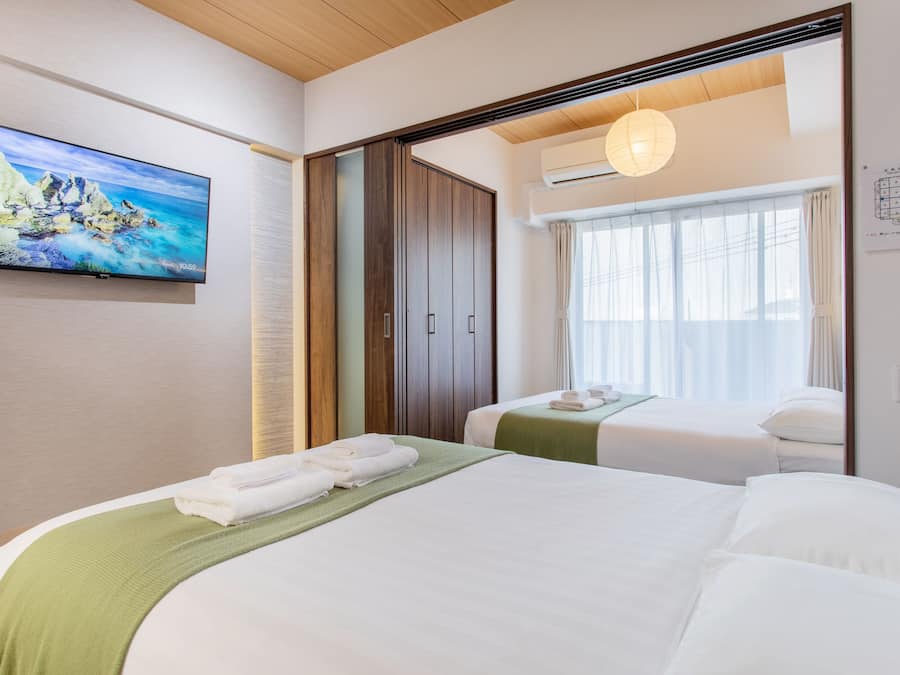 Ett hotellrum med två sängar, en tv, en garderob och ett fönster med gardiner.