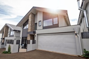 A modern two-story house with a stone accent wall, a garage, and a small patio area. - Stone River Villa 3 | Relaxed Stay | Heated Pool (Margaret River)