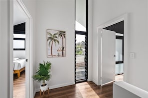 A hallway with a wooden floor, a potted plant, and a framed picture of palm trees. - Stone River Villa 3 | Relaxed Stay | Heated Pool (Margaret River)