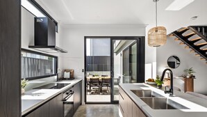 Una cocina moderna con una isla central, un comedor con mesa y sillas, y una escalera que sube a un nivel superior.