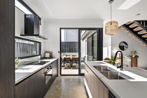 A modern kitchen with a central island, a dining area with a table and chairs, and a staircase leading to an upper level. - Stone River Villa 3 | Relaxed Stay | Heated Pool (Margaret River)