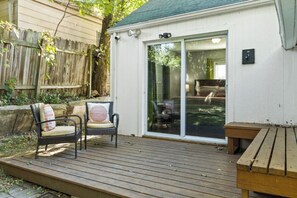 Eine Holzdar Terrasse mit zwei Korbstühlen und einer Bank, einer Schiebetür und einem kleinen Außenbereich mit Holzzaun.