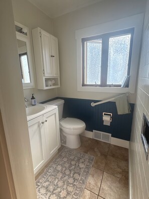 A bathroom with a toilet, sink, mirror, window, and patterned rug.
