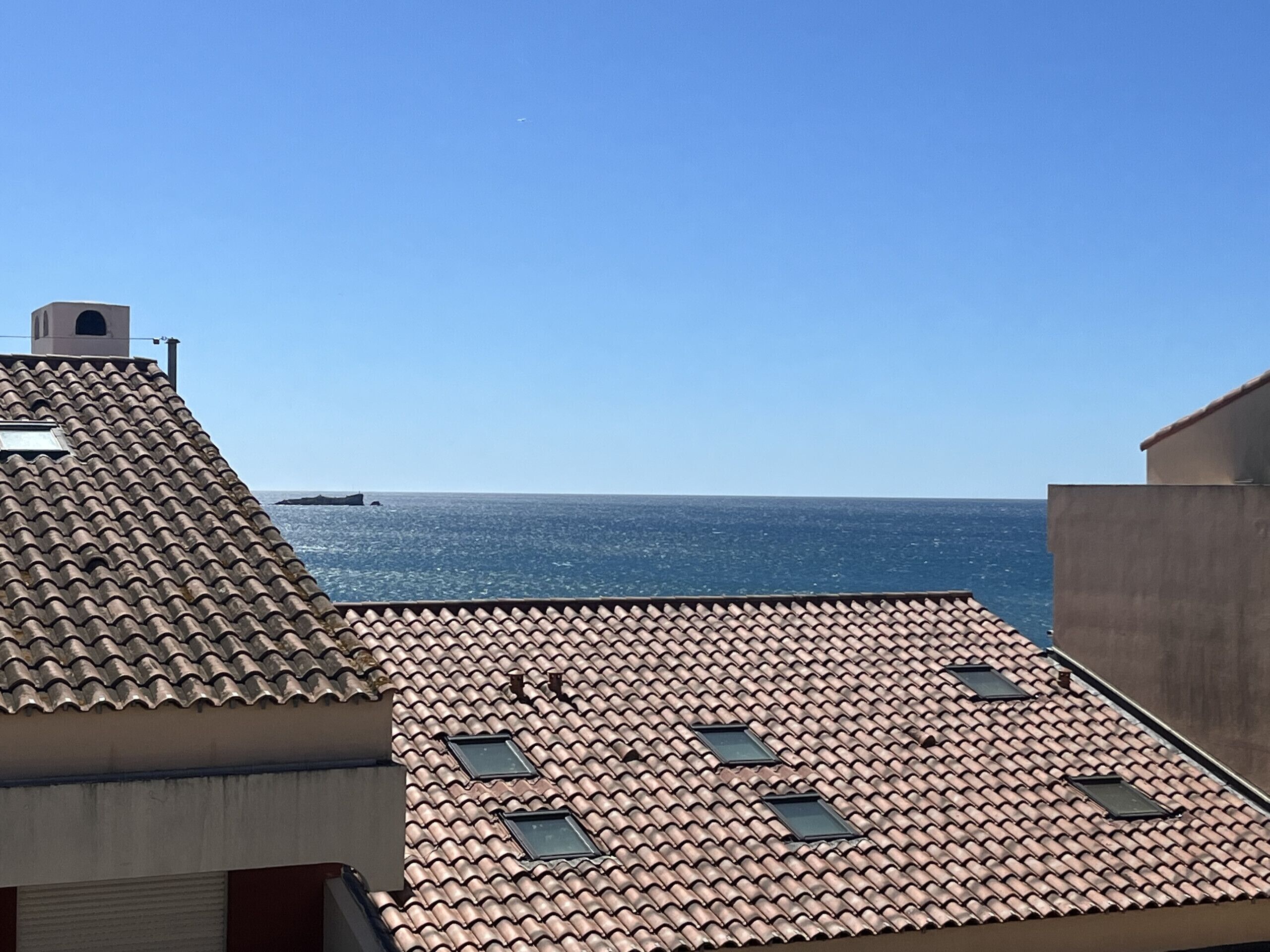 Um terraço com telhas de barro, claraboias e vista para o mar.