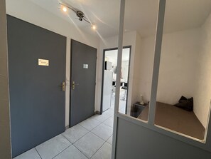 A hallway with two doors, a ceiling fan, and a mirror reflecting a room with a bed and a nightstand. - Capitole, seafront, studio with sleeping alcove for 3 people, 26m2, balcony with partial sea view, air conditioning, private parking (Fréjus)