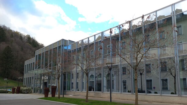 A modern building with a glass facade, a paved entrance area, and a few trees. - Charming studio in the heart of uriage (saint martin d'uriage)