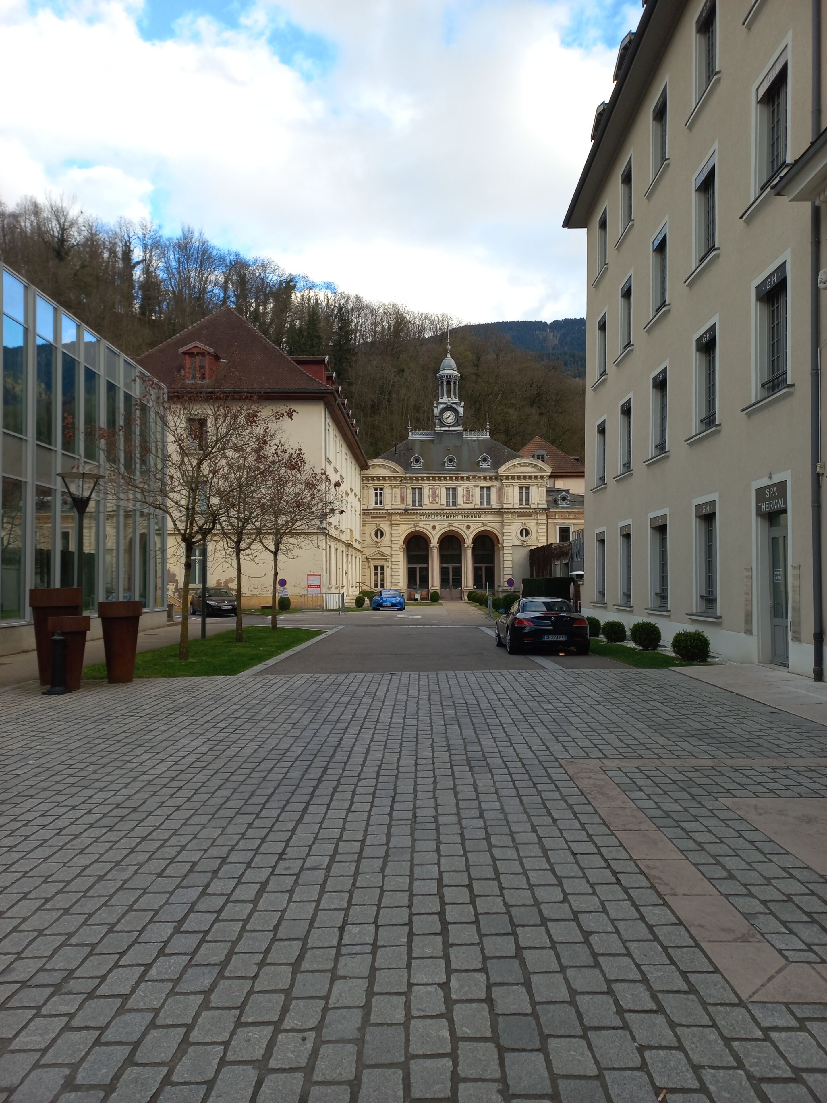 Une cour pavée avec un bâtiment doté d’une tour horlogère et de fenêtres en arc de cercle.