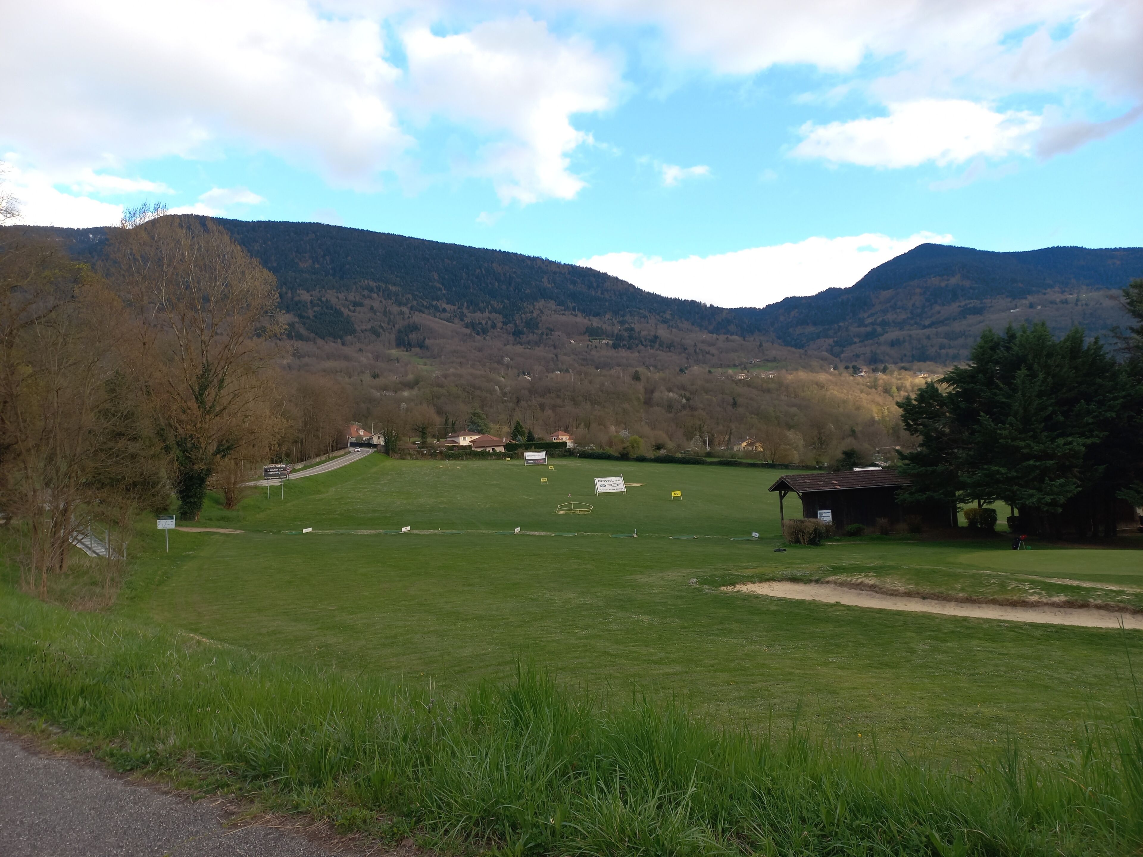 Un paysage rural avec un champ d’herbe, un petit bâtiment et des montagnes en arrière-plan.