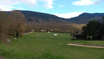 Un paysage rural avec un champ d’herbe, un petit bâtiment et des montagnes en arrière-plan.