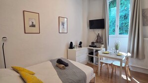 A bedroom with a bed, bedside table, desk, chair, and a window with curtains. - Charming studio in the heart of uriage (saint martin d'uriage)