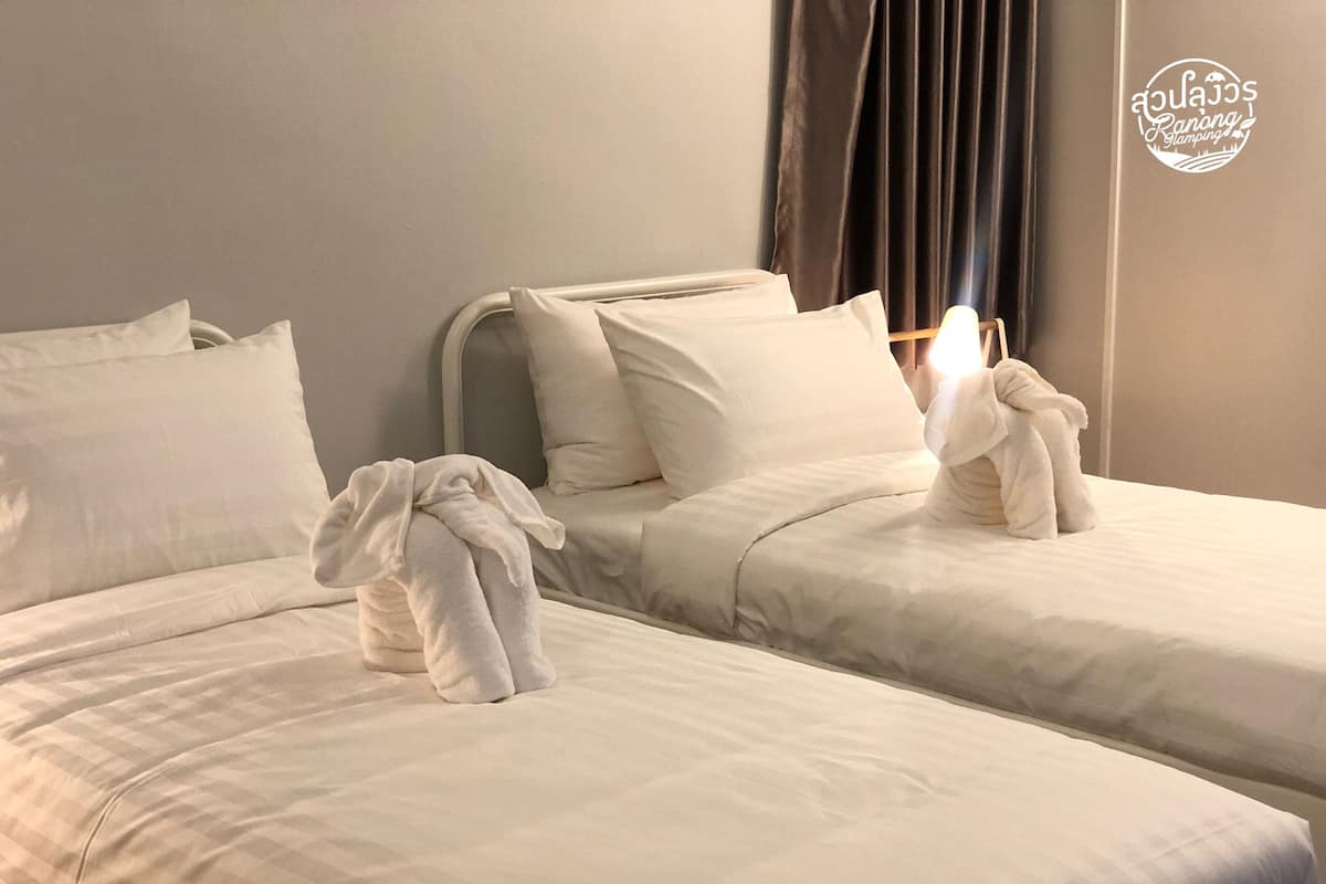 Two beds with white linens, a headboard, and a window with curtains.