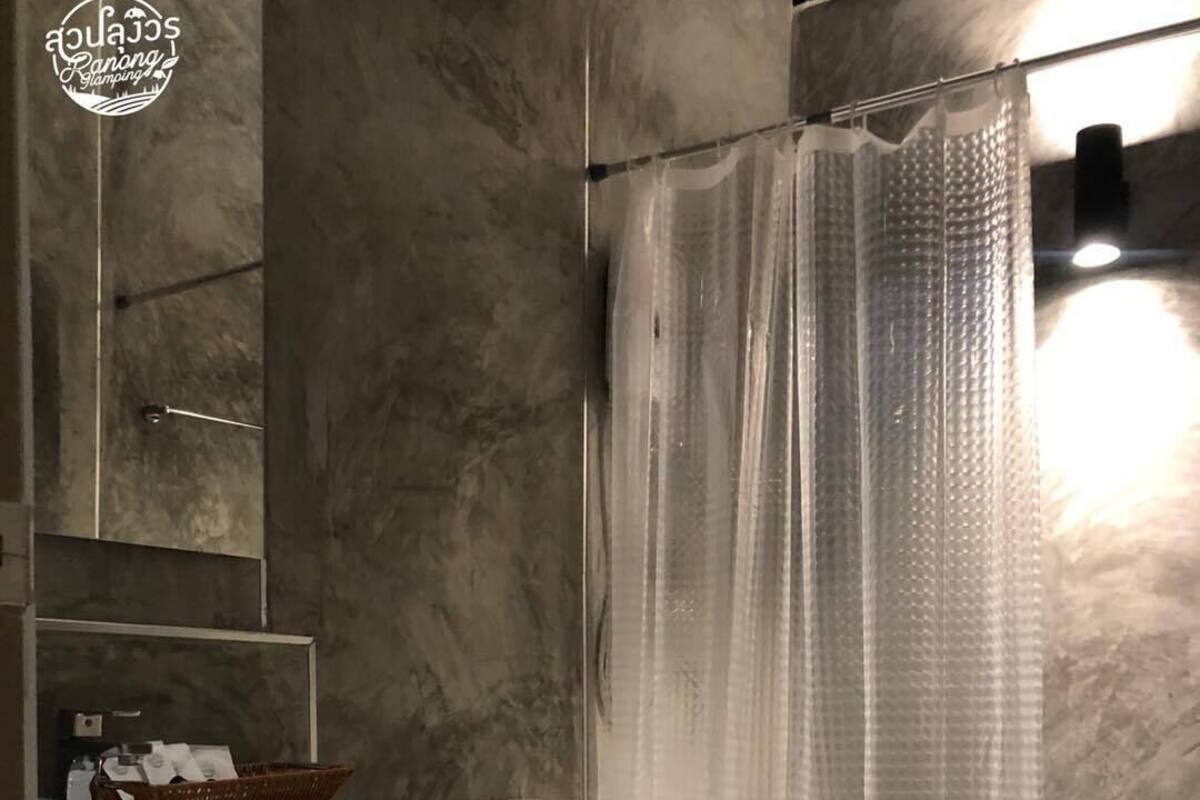A bathroom with a marble wall, a white sink, a toilet, and a shower curtain.