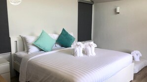 Una cama bien hecha con sábanas blancas, una almohada verde azulada y un juego de toallas sobre la cama.