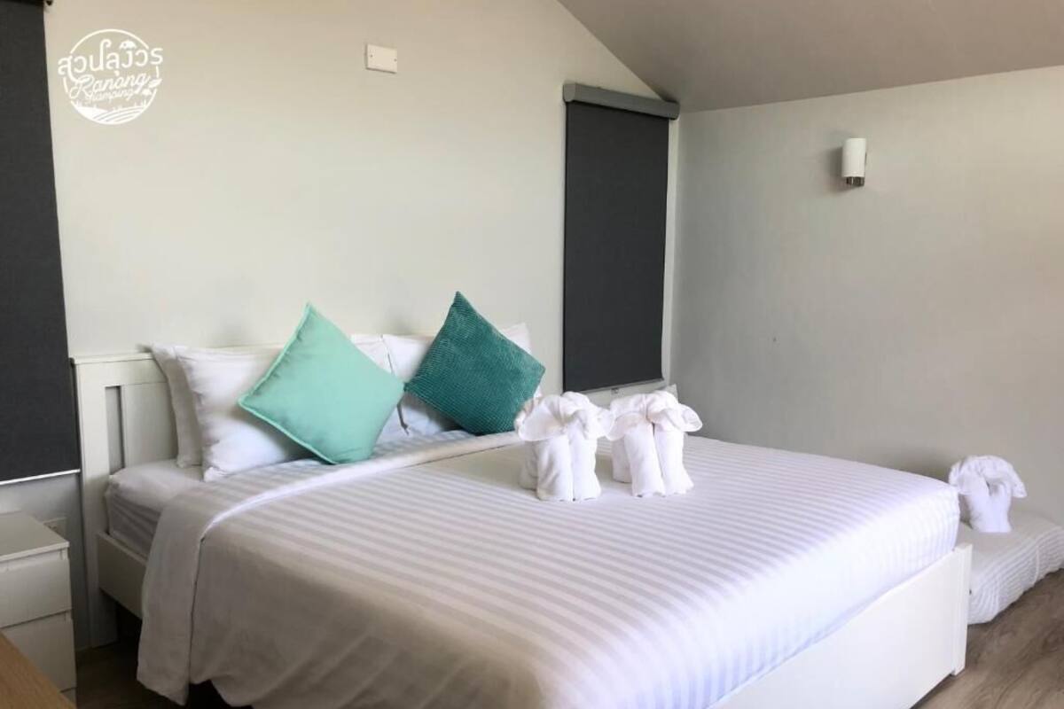 A neatly made bed with white linens, a teal pillow, and a set of towels on the bed.