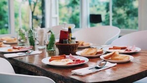 Una mesa de comedor con platos de comida, una cesta con salsas y una ventana con vista a follaje.