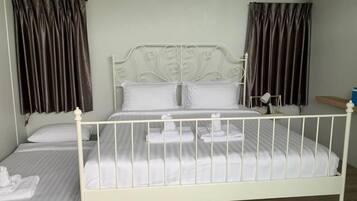 A twin bed with a white metal frame, a single bed with a white mattress, and a nightstand with a lamp.