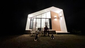 Un edificio moderno con ventanas amplias y techo plano, una persona sentada en un banco, y dos perros en el suelo.