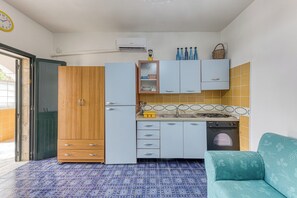 Eine kleine Küche mit Kühlschrank, Herd, Backofen und Spüle. Im Raum befindet sich ein Holzschrank und ein blaues Sofa.