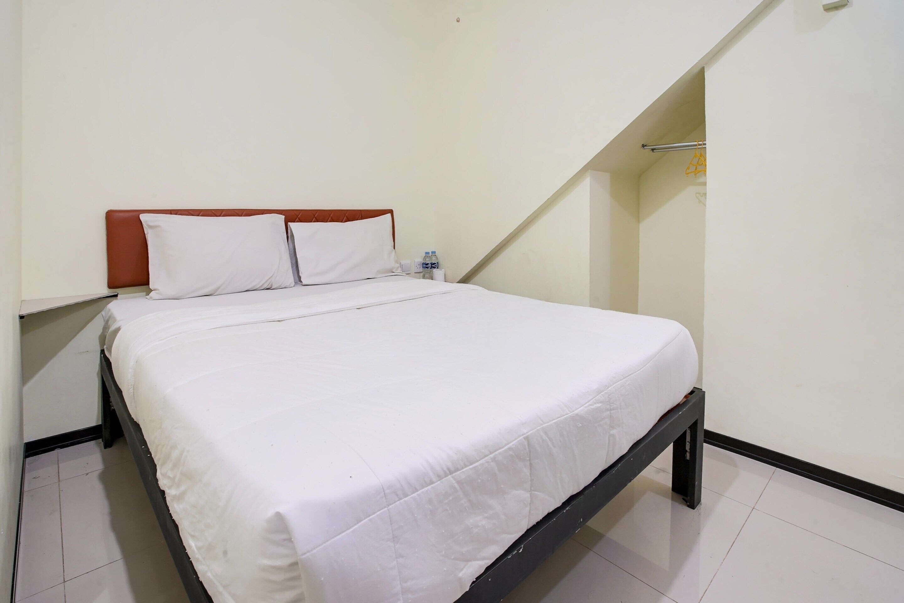 A single bed with a white mattress and two pillows, a nightstand with a water bottle, and a sloped ceiling.
