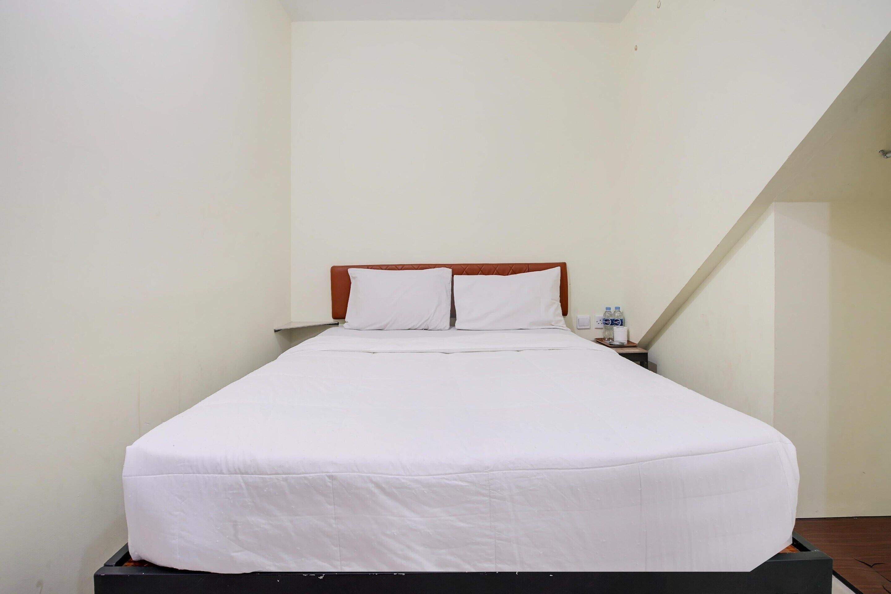 Un lit simple avec une literie blanche, dans une pièce aux murs unis et au plafond en pente.
