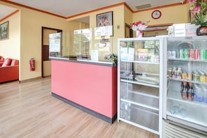 Zona de recepción con un mostrador rojo, una vitrina de vidrio con bebidas y un reloj en la pared.