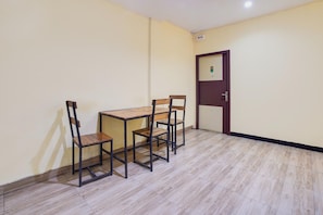 A room with a wooden table and four chairs, a door with a security camera, and a tiled floor.