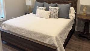 A bedroom with a large bed, a wooden headboard, two bedside tables with lamps, and a round table with a lamp.