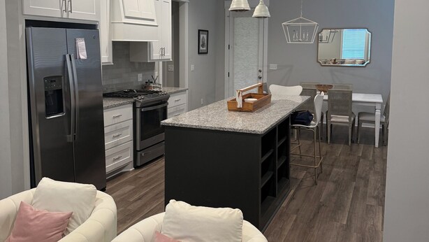 A modern kitchen with white cabinets, a stainless steel refrigerator, a dining area with a white table and chairs, and a central island with a mirror above.