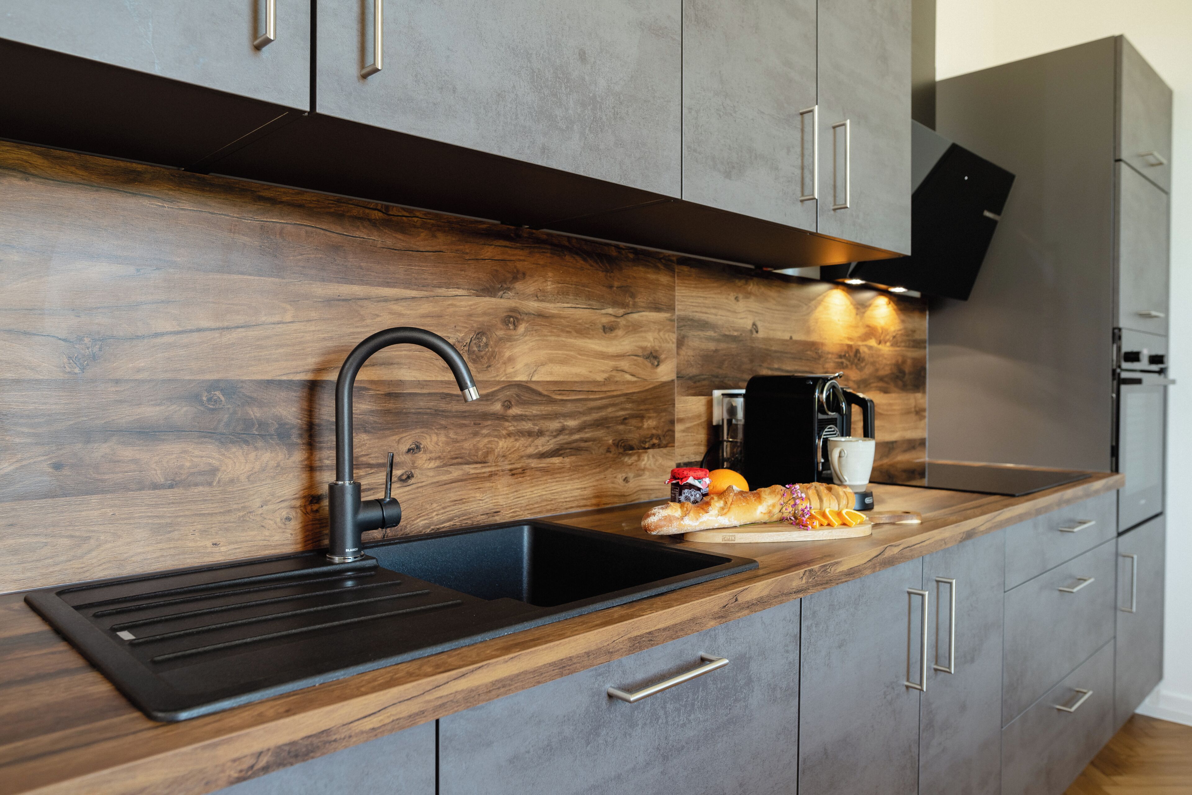 Eine moderne Küche mit einer Holz Arbeitsplatte, einem schwarzen Spülbecken und einem eingebauten Backofen.