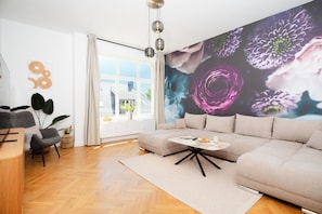 A modern living room with a large sofa, a coffee table, and a large window with curtains.
