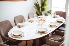 Ett matbord dukat med tallrikar, glas och en skål med frukt, omgivet av stoppade stolar.