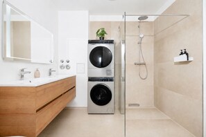 Ein modernes Badezimmer mit einem Holzbadezimmer-Möbelstück, einem großen Spiegel, einer an der Wand befestigten Waschmaschine und einer Duschkabine aus Glas.