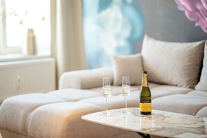 A modern living room with a sofa, a small table, two glasses, and a bottle of Valdo wine.