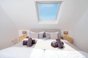 Ein ordentlich gemachtes Bett mit Handtüchern, einer Nachttischlampe und einem Fenster darüber.