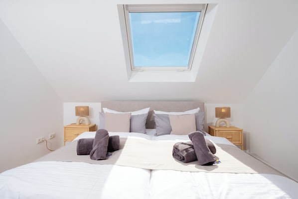 A neatly made bed with towels, a bedside lamp, and a window above the bed.