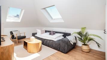 Ein modernes Schlafzimmer mit Dachfenster, einer Couch, einem Sessel, einem runden Holztisch und einem Topfpflanzen.