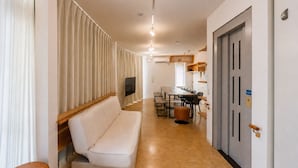 Un pasillo con sofá, mesa de comedor con sillas, televisor montado en la pared y una puerta con manija.