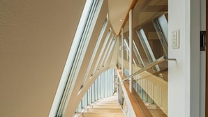 Un interior moderno con una escalera, barandillas de vidrio e iluminación empotrada en el techo.
