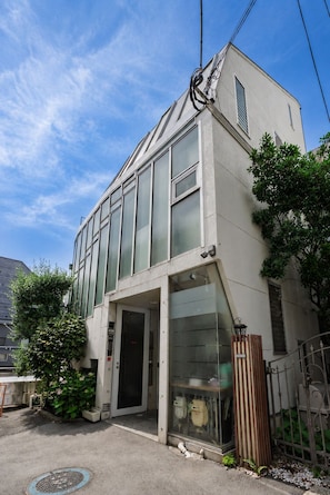Un edificio con una amplia fachada de vidrio, una entrada visible y un pequeño árbol en la parte delantera.