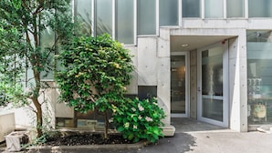 Una entrada de edificio con un pequeño árbol, una jardinera de concreto y un portón de metal.