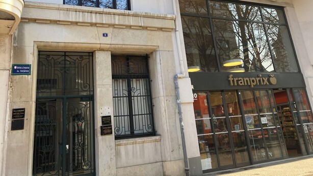 En bygning med flere etager, en stor indgang, et skilt med 'PARIS' og en butik med skiltet 'franprix'.