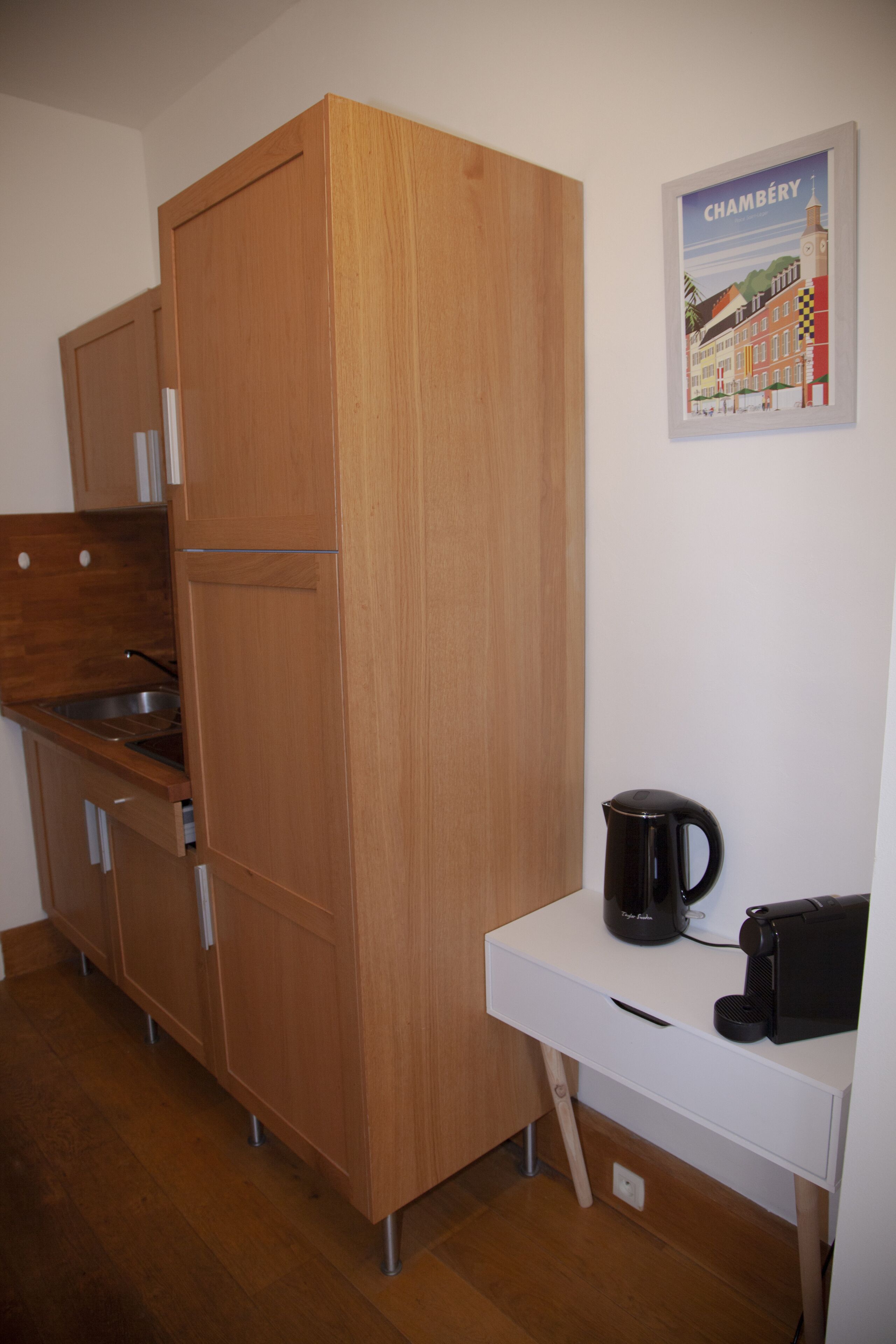 Cuina compacta amb armaris de fusta, taulell blanc, bullidor d'aigua i cafetera.