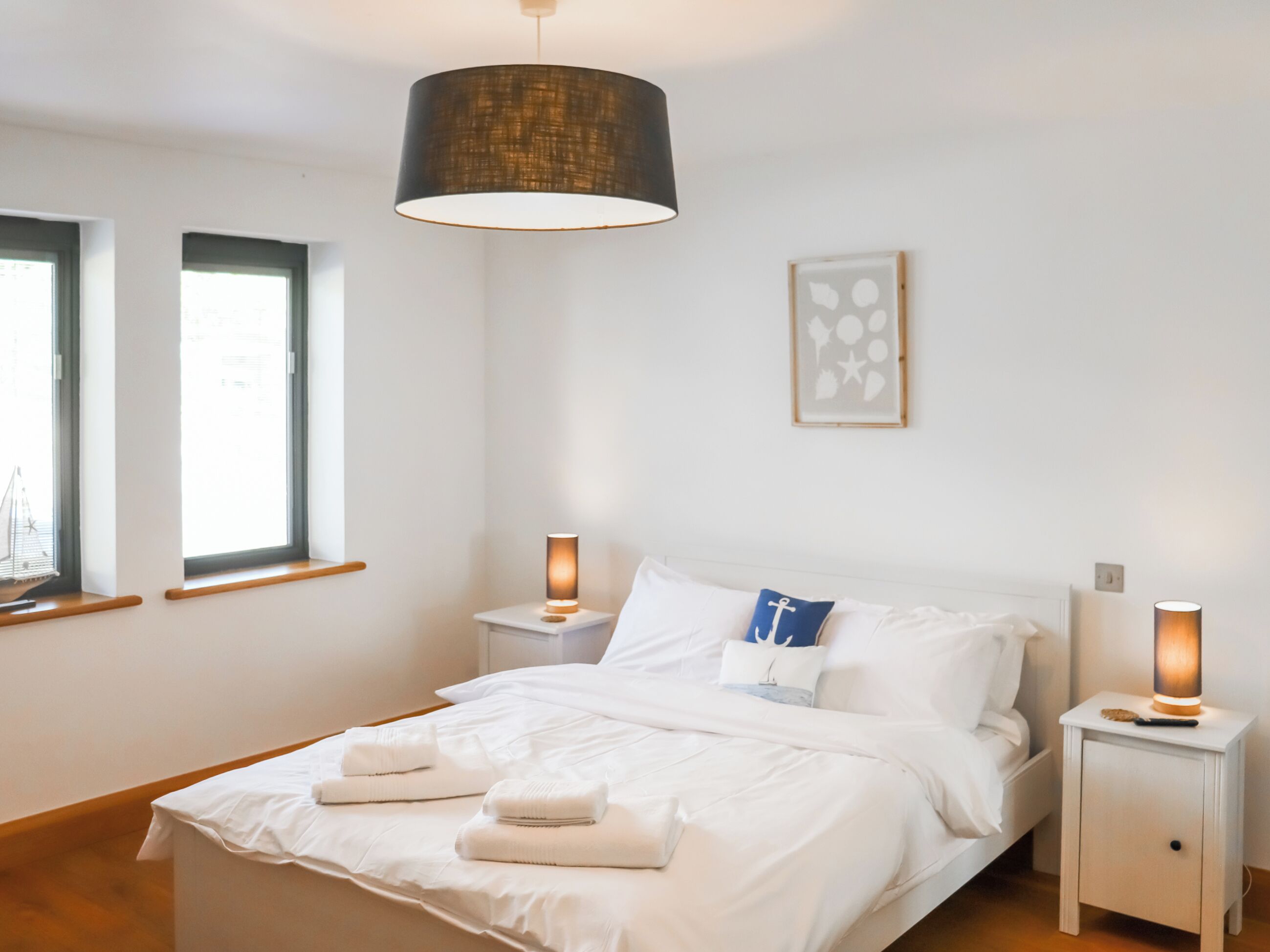 Een slaapkamer met een bed, nachtlampjes, een raam en een kunstwerk aan de muur.