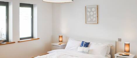 Een slaapkamer met een bed, nachtlampjes, een raam en een kunstwerk aan de muur.