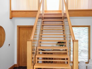 Eine Holztreppe mit Glastrennwand, die zu einer höheren Etage führt.